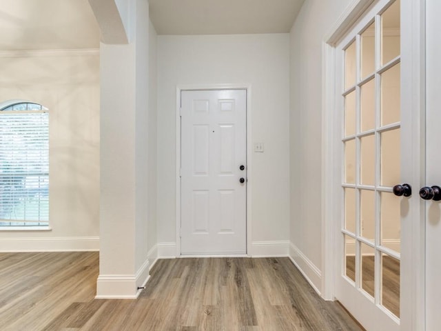 foyer entrance featuring arched walkways, light wood-style flooring, and baseboards