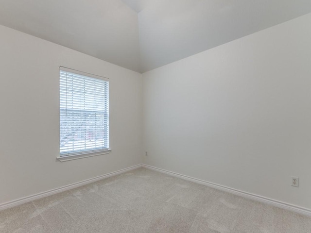 spare room featuring lofted ceiling, baseboards, and light colored carpet