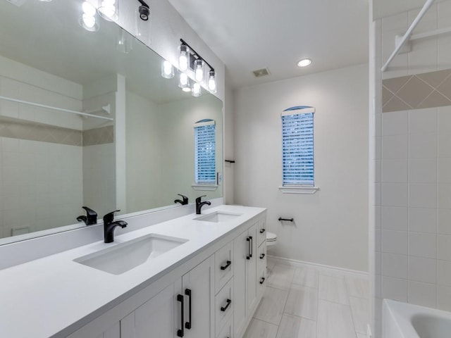 full bathroom with double vanity, a sink, toilet, and baseboards