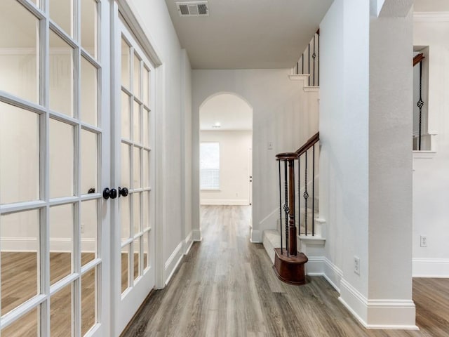 hall with arched walkways, visible vents, wood finished floors, baseboards, and stairs