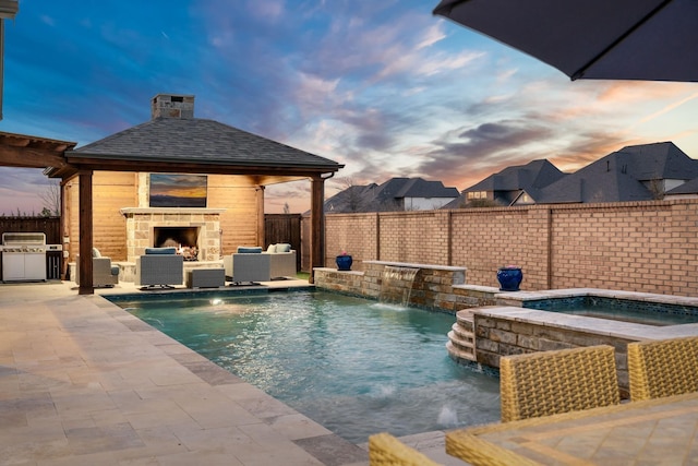 pool at dusk with an outdoor stone fireplace, a patio, an outdoor kitchen, area for grilling, and a fenced backyard