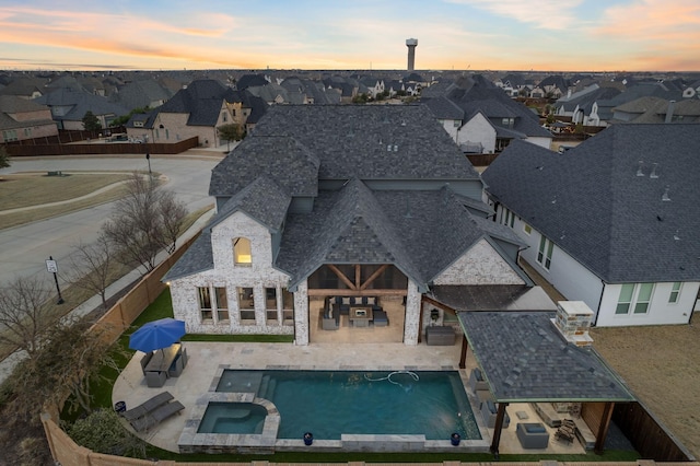 back of property at dusk with stone siding, a patio area, a residential view, and a pool with connected hot tub