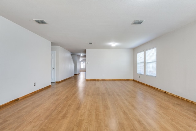 unfurnished living room featuring visible vents, light wood-style floors, and baseboards