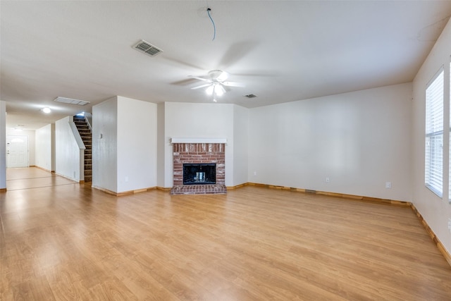 unfurnished living room with ceiling fan, visible vents, light wood finished floors, stairs, and a fireplace