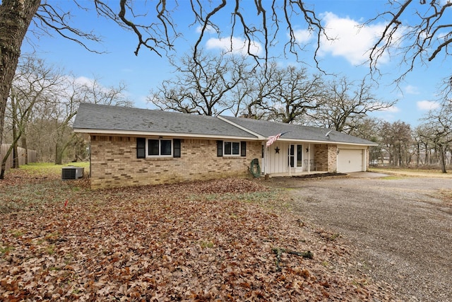 view of front of home featuring dirt driveway, a chimney, an attached garage, central AC, and brick siding