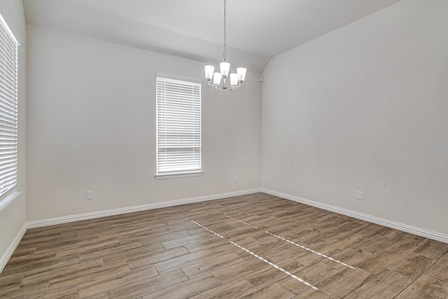 unfurnished room with baseboards, a chandelier, vaulted ceiling, and wood finished floors