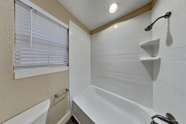 bathroom featuring a textured wall, washtub / shower combination, and toilet