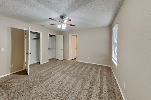 unfurnished bedroom with a textured ceiling, visible vents, baseboards, multiple closets, and carpet