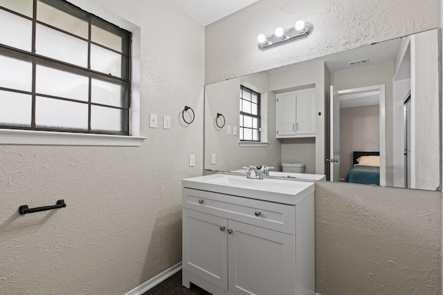 ensuite bathroom featuring a textured wall, vanity, connected bathroom, visible vents, and toilet