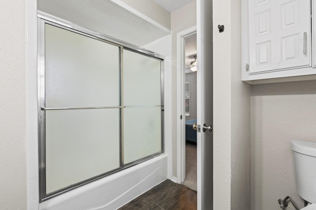 bathroom featuring toilet, bath / shower combo with glass door, wood finished floors, and a textured wall