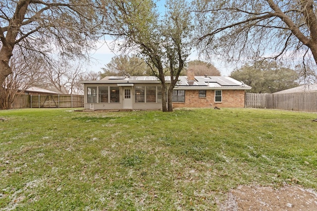 rear view of house featuring a sunroom, a fenced backyard, a lawn, and solar panels