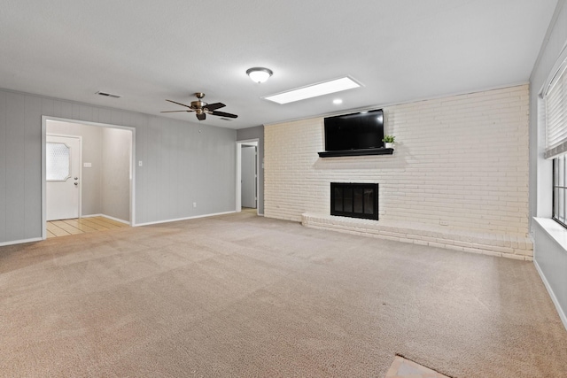 unfurnished living room with light colored carpet, brick wall, visible vents, a brick fireplace, and ceiling fan