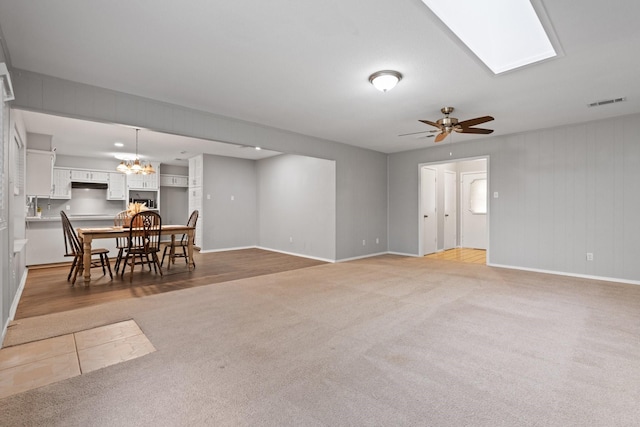 living area featuring light colored carpet, a skylight, visible vents, baseboards, and ceiling fan with notable chandelier