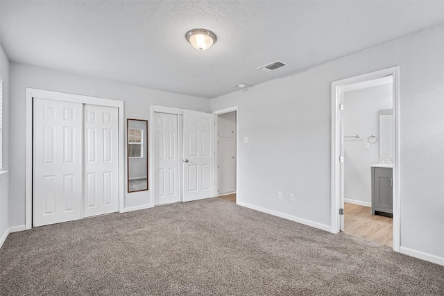 unfurnished bedroom featuring baseboards, visible vents, light carpet, and multiple closets