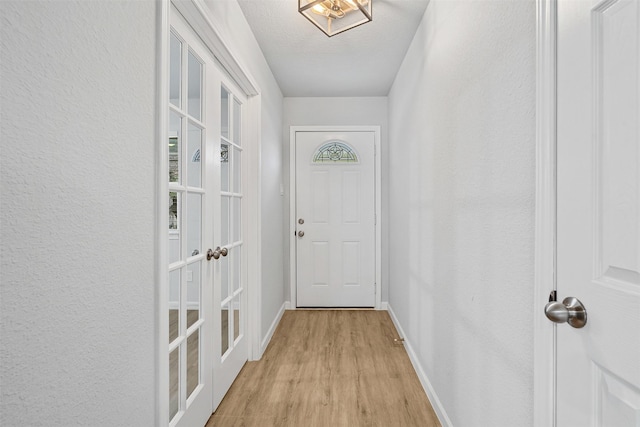 doorway to outside with baseboards, a textured wall, a textured ceiling, french doors, and light wood-style floors