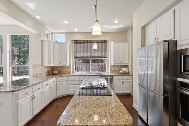 kitchen with decorative light fixtures, a kitchen island, white cabinetry, and appliances with stainless steel finishes