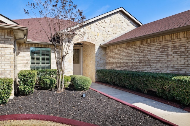 entrance to property featuring stone siding, a shingled roof, and brick siding