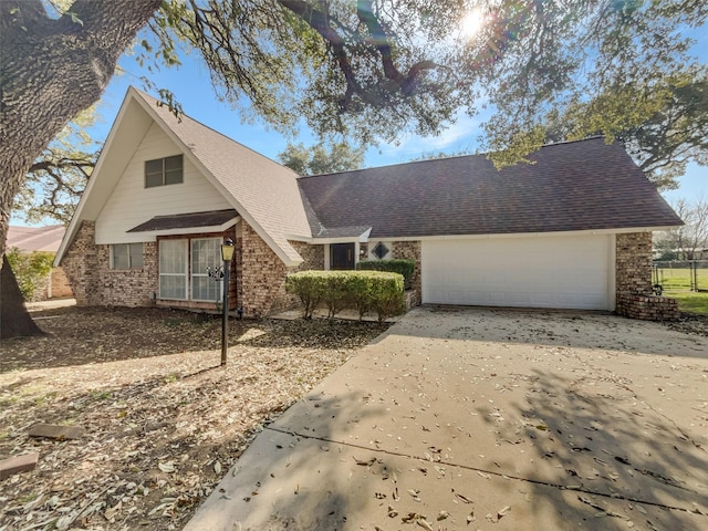 a-frame style home with a garage, concrete driveway, brick siding, and a shingled roof