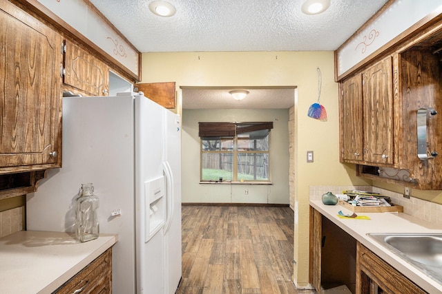 kitchen with a sink, light countertops, white fridge with ice dispenser, and brown cabinetry