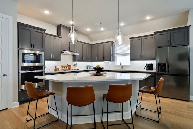 kitchen with pendant lighting, light countertops, appliances with stainless steel finishes, a kitchen island, and under cabinet range hood