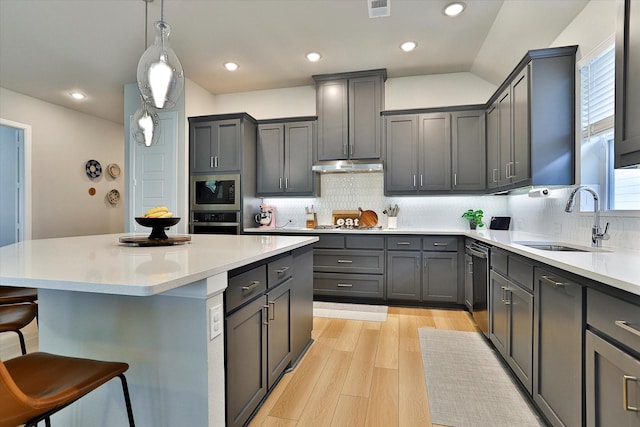 kitchen with light countertops, gray cabinetry, under cabinet range hood, stainless steel oven, and a sink