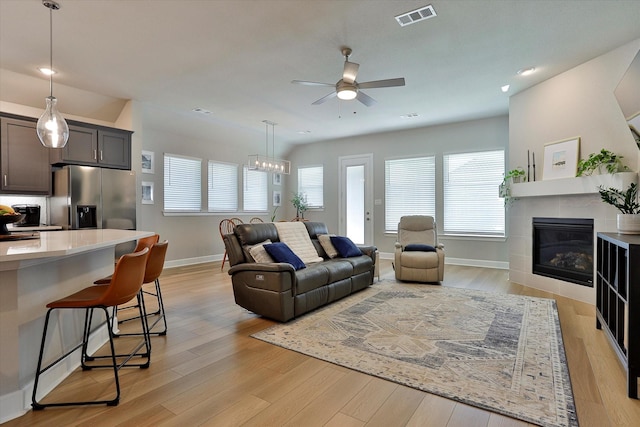 living area with ceiling fan, visible vents, baseboards, light wood-style floors, and a tiled fireplace