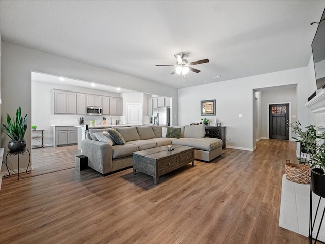 living area with light wood-type flooring, a ceiling fan, and baseboards