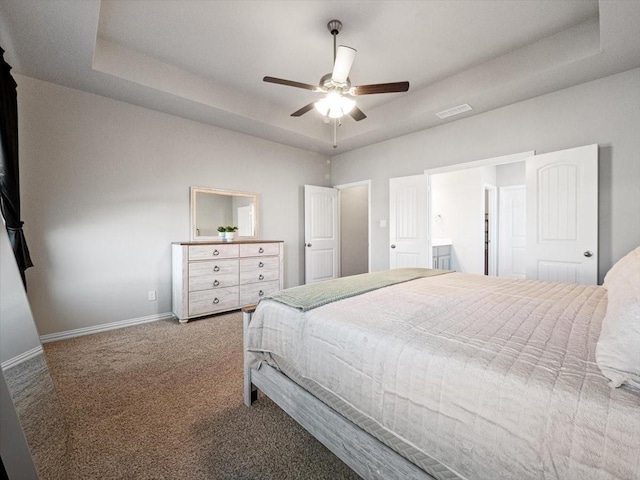 bedroom featuring ceiling fan, visible vents, baseboards, a tray ceiling, and carpet