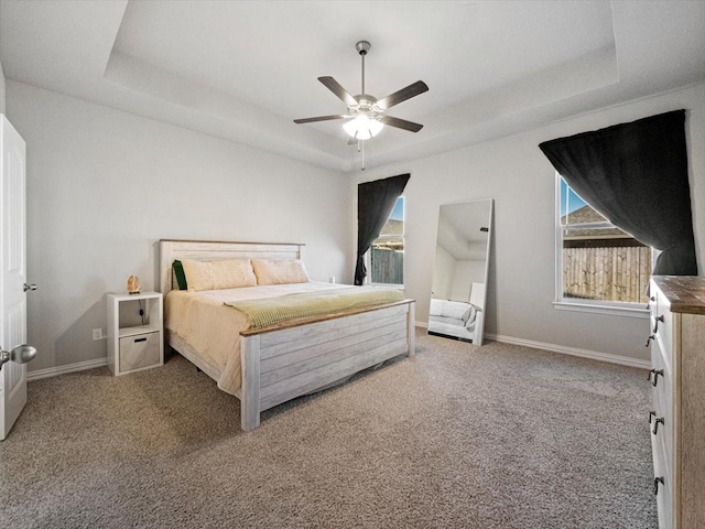 carpeted bedroom with ceiling fan, a tray ceiling, and baseboards