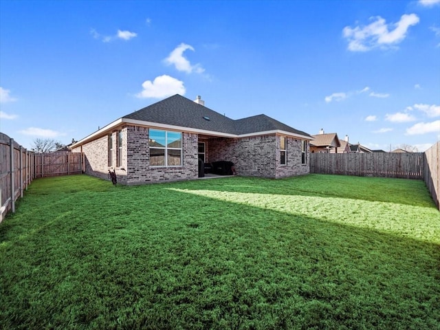 back of house with a fenced backyard, a yard, a chimney, and brick siding