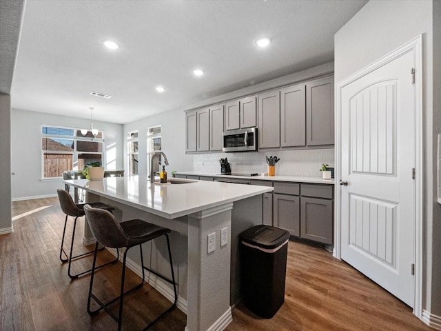 kitchen featuring pendant lighting, light countertops, stainless steel microwave, a sink, and an island with sink