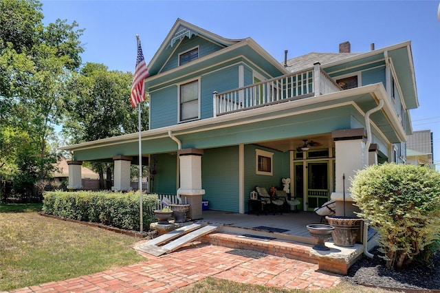 back of property with a lawn, a chimney, a balcony, and a ceiling fan