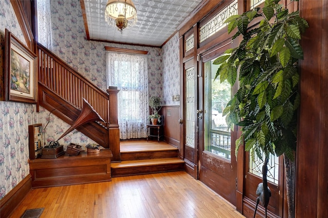 foyer featuring wallpapered walls, visible vents, a wainscoted wall, an ornate ceiling, and crown molding