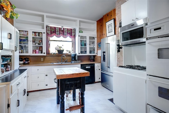 kitchen with light countertops, appliances with stainless steel finishes, glass insert cabinets, white cabinets, and a sink