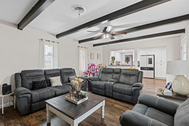 living area with dark wood-type flooring, visible vents, beamed ceiling, and a ceiling fan