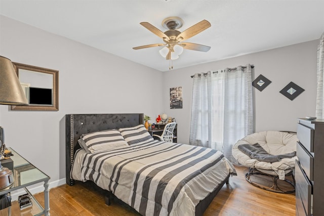 bedroom featuring multiple windows, wood finished floors, a ceiling fan, and baseboards