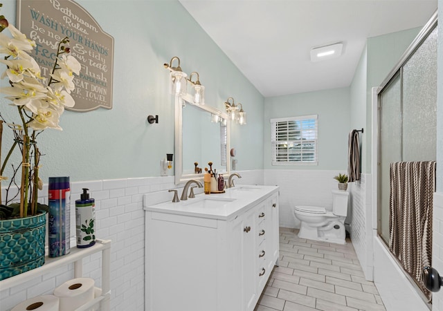 full bathroom with tile walls, bath / shower combo with glass door, toilet, wainscoting, and a sink