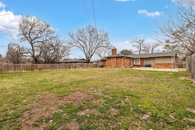 view of yard with an attached garage, driveway, a fenced backyard, and a patio