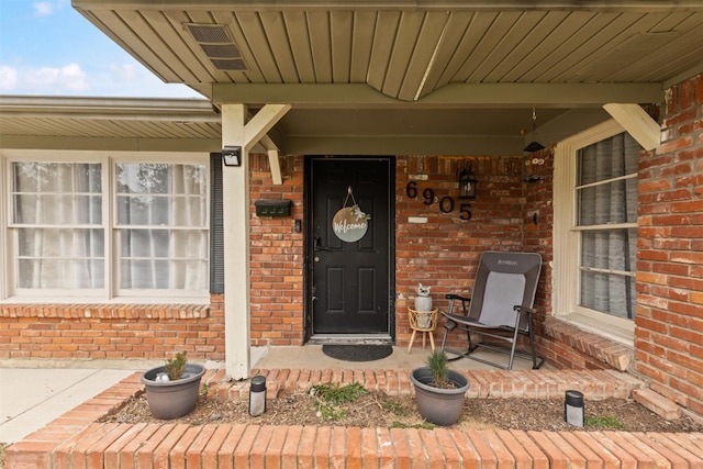 doorway to property with a porch and brick siding