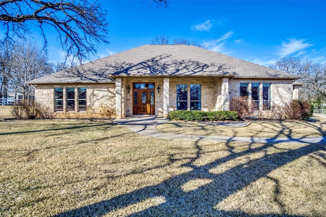 view of front of house with stone siding, a shingled roof, and a front lawn