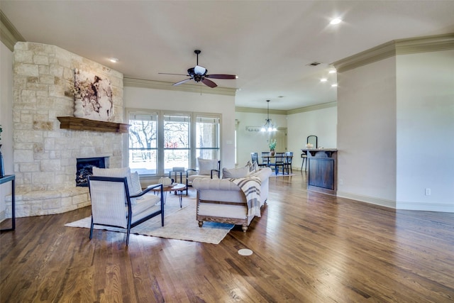 living area featuring a stone fireplace, a ceiling fan, baseboards, ornamental molding, and dark wood-style floors