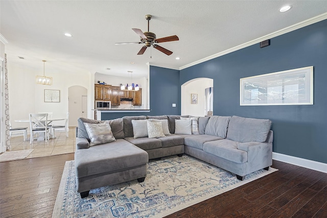 living area featuring baseboards, arched walkways, ornamental molding, wood finished floors, and ceiling fan with notable chandelier