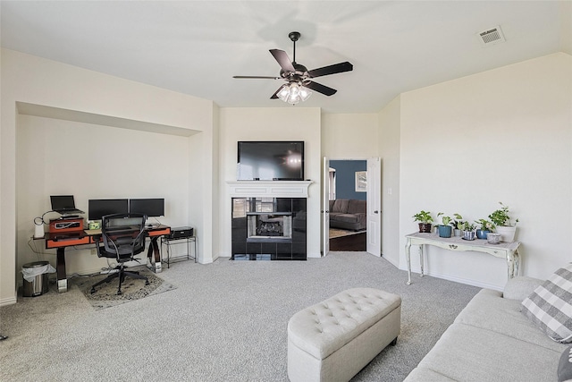 carpeted office space with baseboards, visible vents, a ceiling fan, and a tile fireplace