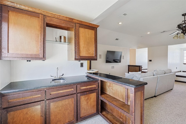 kitchen with dark countertops, a ceiling fan, open floor plan, and a sink