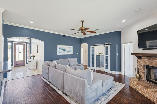 living room featuring a brick fireplace, a barn door, arched walkways, and wood finished floors