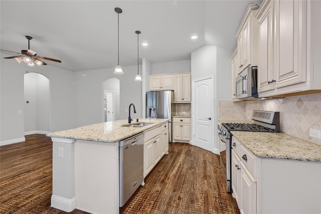 kitchen featuring arched walkways, a kitchen island with sink, a sink, hanging light fixtures, and appliances with stainless steel finishes