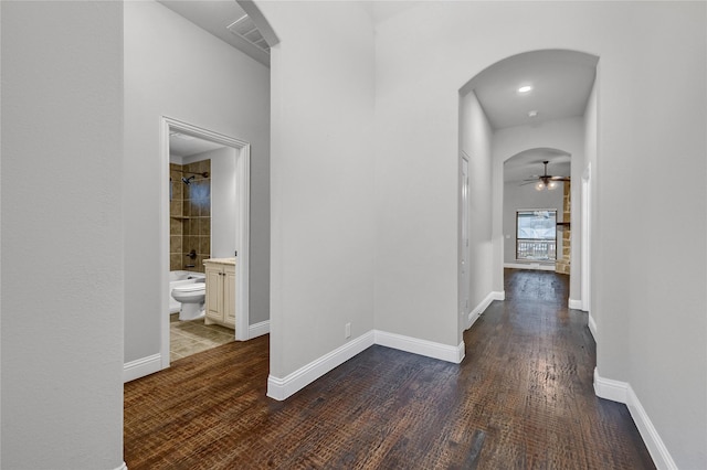 hallway featuring arched walkways, visible vents, dark wood finished floors, and baseboards