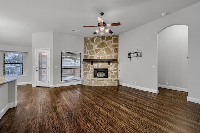 unfurnished living room featuring visible vents, arched walkways, baseboards, ceiling fan, and a fireplace