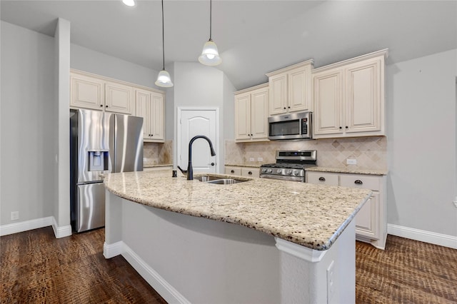 kitchen featuring appliances with stainless steel finishes, a center island with sink, hanging light fixtures, and light stone countertops