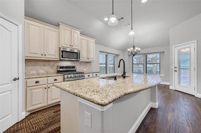 kitchen with light stone counters, stainless steel appliances, a sink, hanging light fixtures, and a center island with sink